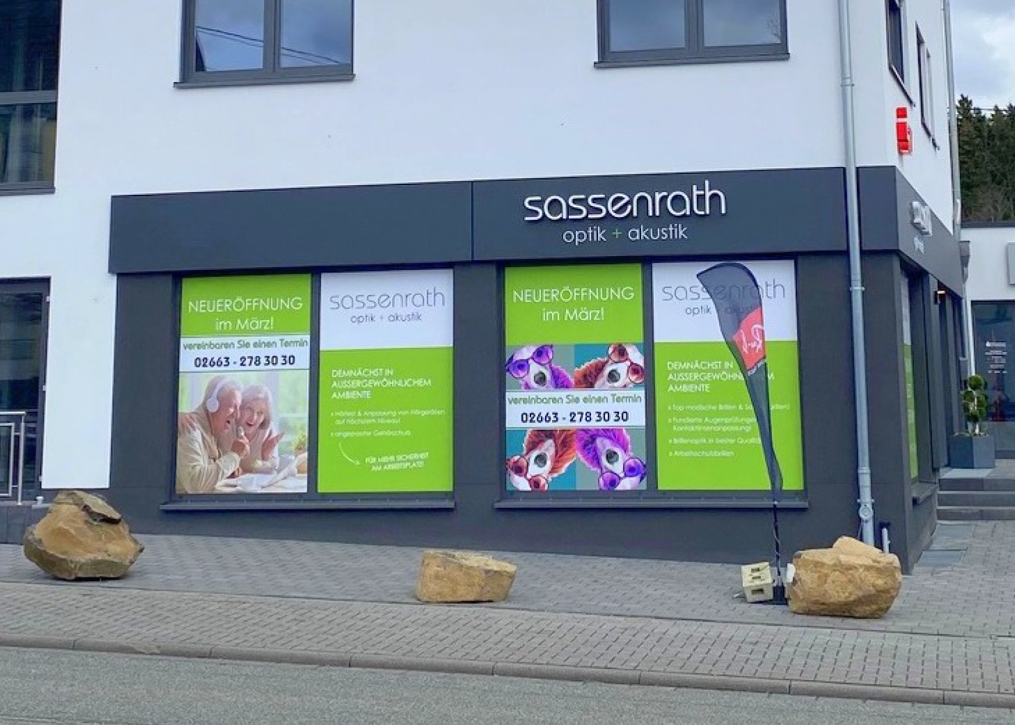 Schaufenster von Sassenrath optik + akustik mit Plakaten „NEUERÖFFNUNG im März“, Ankündigung einer Neueröffnung im März und Angabe der Kontaktnummer 02663-2783030, Teil der regionalen Gewerbegemeinschaft Westerburg.