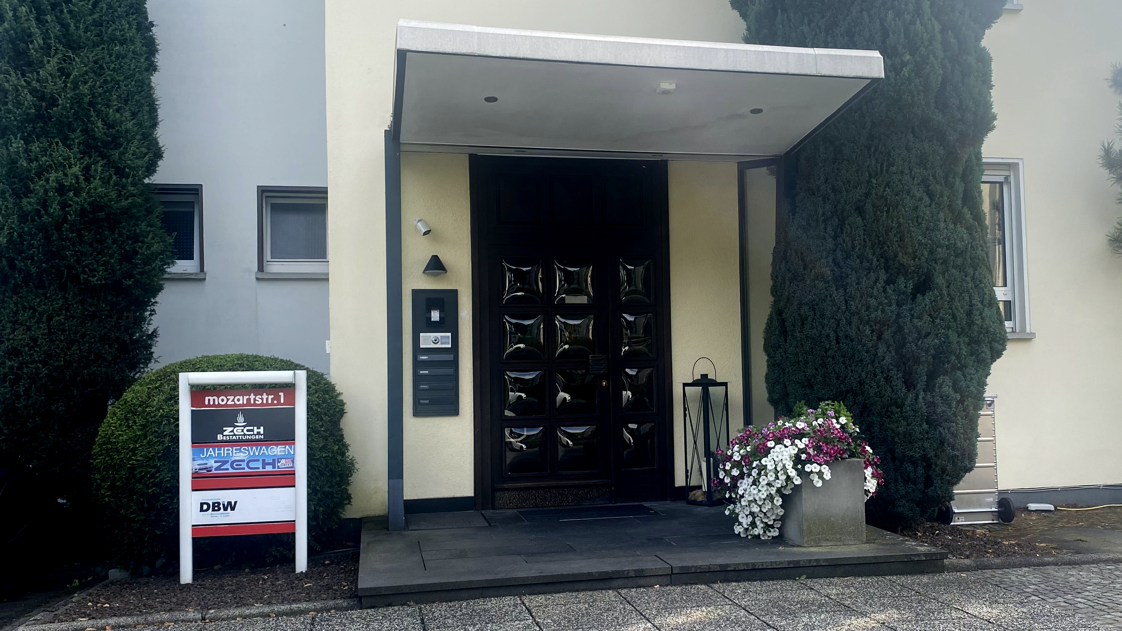 Eingangsbereich eines Gebäudes an der Mozartstraße 1 mit Schild für ZECH Bestattungen und Blumen, symbolisch für die lokalen Unternehmen im Westerburger Land.