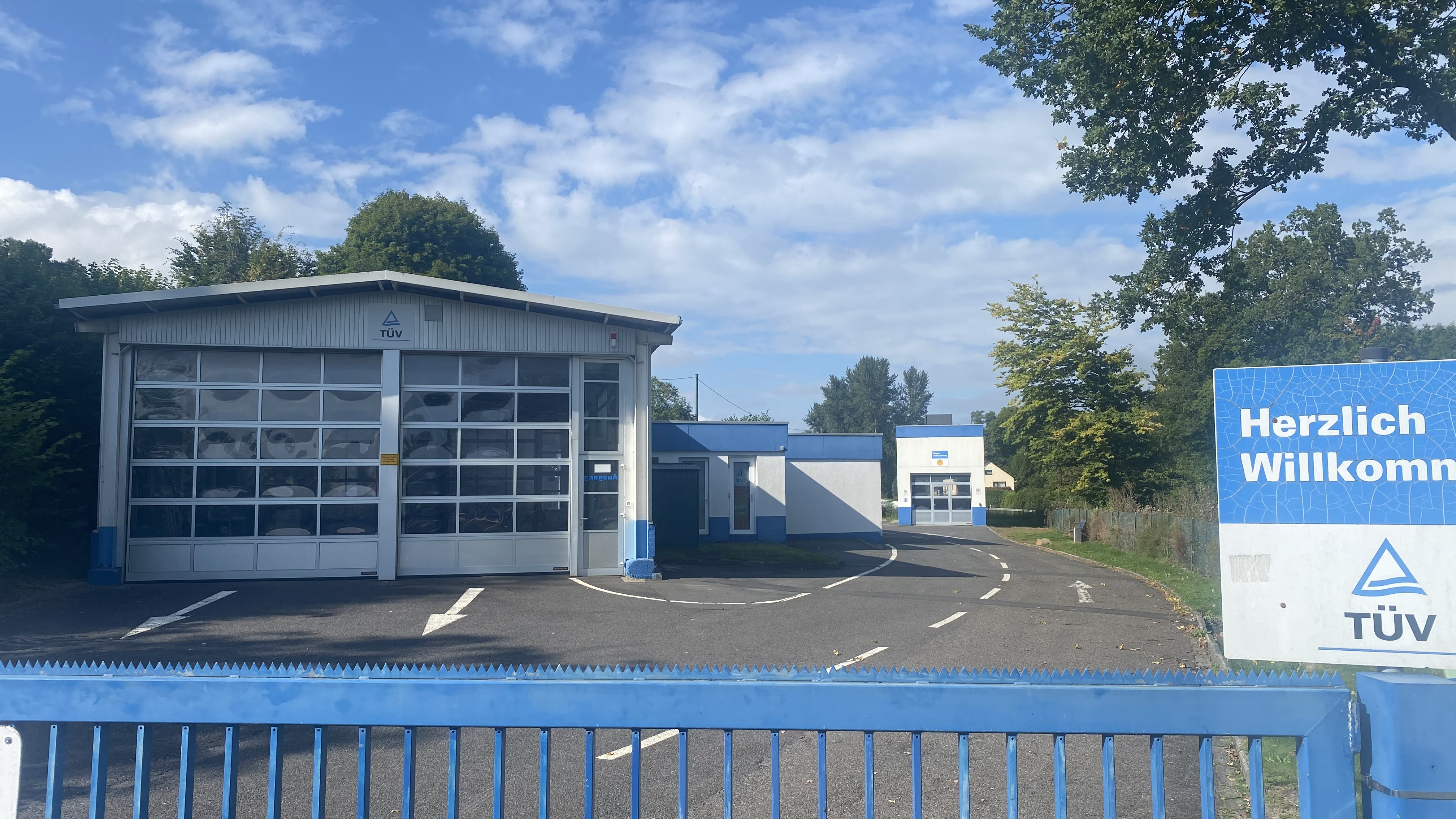 TÜV-Gebäude mit blau-weißer Fassade, „Herzlich Willkommen“-Schild und Parkplatz in der Verbandsgemeinde Westerburg, symbolisierend den lokalen Gewerbe- und Wirtschaftsstandort.