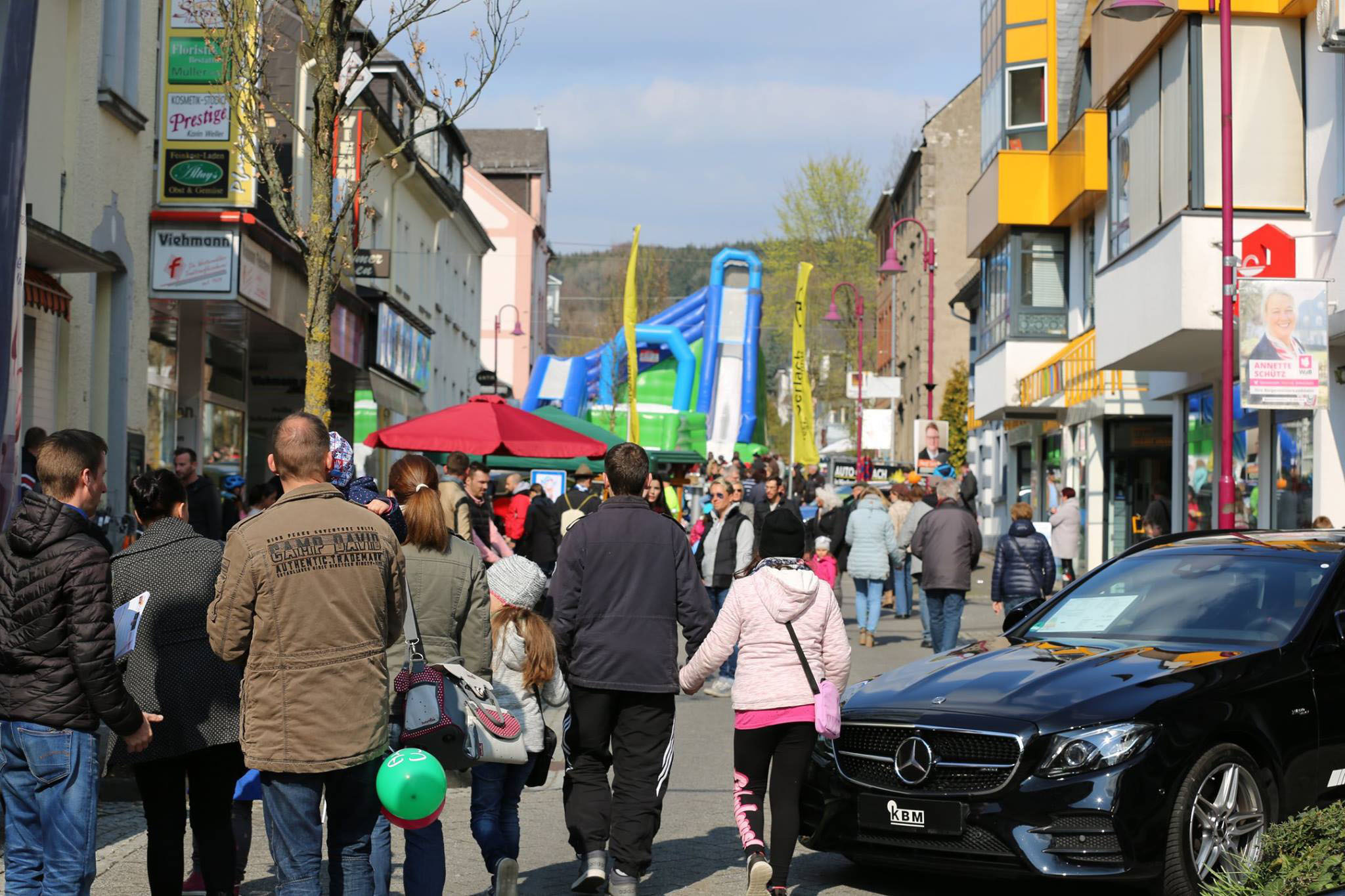 Eine belebte Straße in Westerburg an einem Sonntag – mit Fußgängern, Geschäften, einer aufblasbaren Spielattraktion und einem schwarzen Mercedes –, die die lebhafte Atmosphäre einer vom Gewerbeverein Westerburg organisierten Veranstaltung einfängt, welche lokale Unternehmen und familienfreundliche Aktivitäten fördern soll.