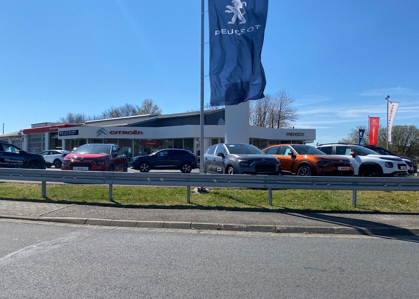 Autohaus Frensch GmbH zeigt Peugeot- und Citroën-Autos in der Ausstellung vor einem hellen Gebäude unter klarem blauem Himmel.
