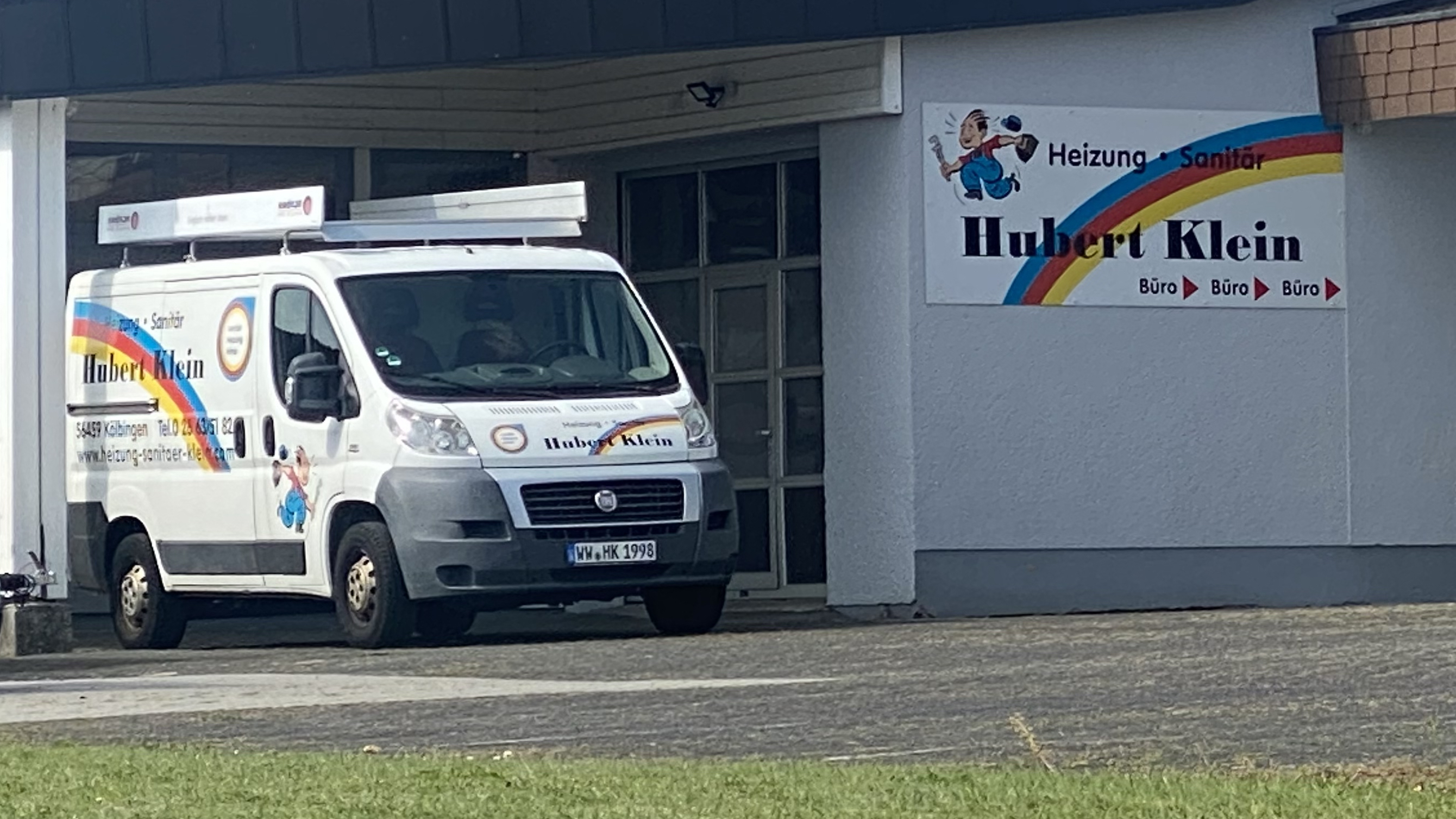 Firmenwagen von Hubert Klein (Heizung · Sanitär) geparkt vor dem Bürogebäude mit Firmenlogo und Regenbogen-Symbol.