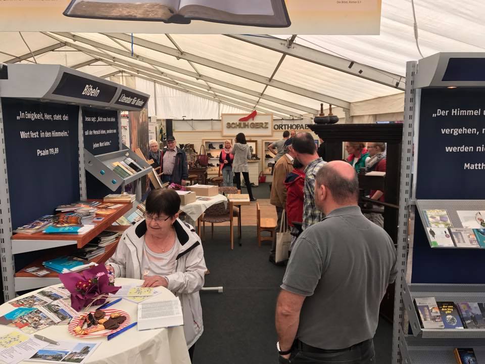 Buchstand mit Bibeln bei der Hui Wäller Messe des Gewerbevereins Westerburg unter einem Zelt, wo Besucher umsehen.