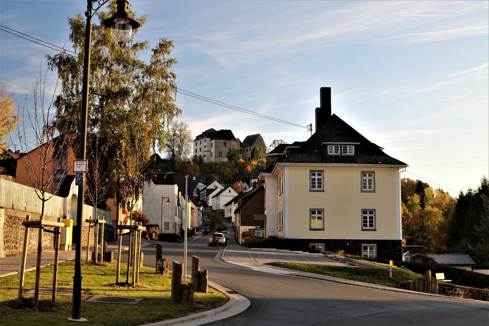 Ansicht einer idyllischen Dorfstraße in Westerburg mit einer Burg auf dem Hügel, traditionellen Häusern und Herbstbäumen, die den ländlichen Charme und die Attraktivität des Wirtschaftsstandorts Westerburger Land unterstreichen.