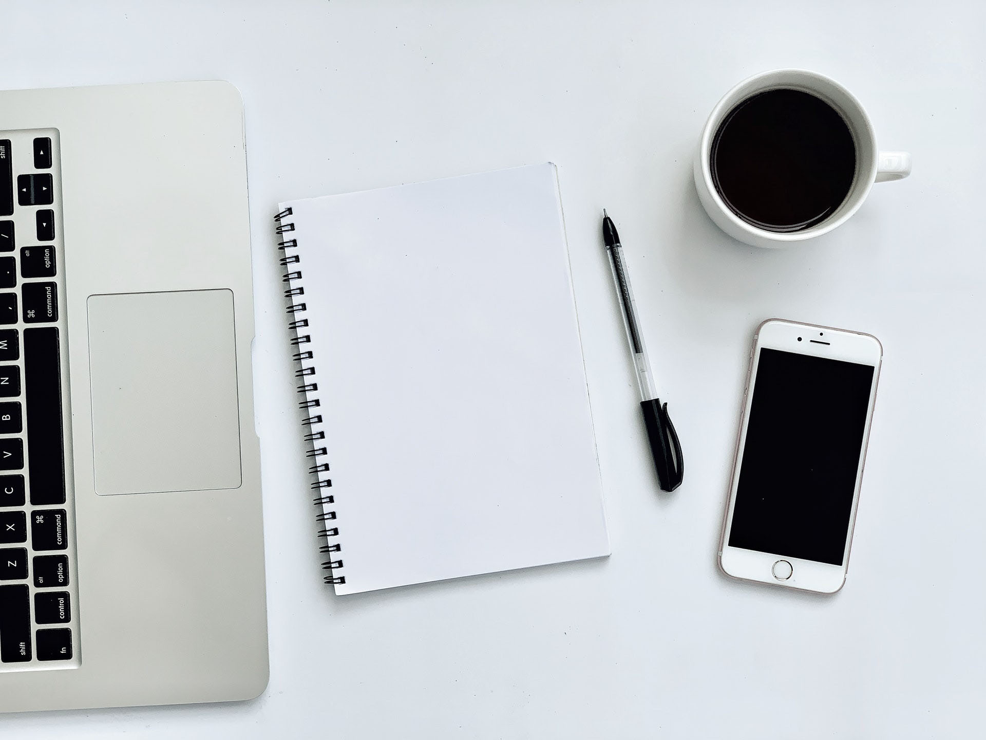 Ein moderner Arbeitsplatz mit Laptop, Spiralblock, Stift, Kaffeetasse und Smartphone auf weißem Hintergrund, repräsentativ für die professionelle Unterstützung lokaler Unternehmen durch den Gewerbeverein Westerburg.