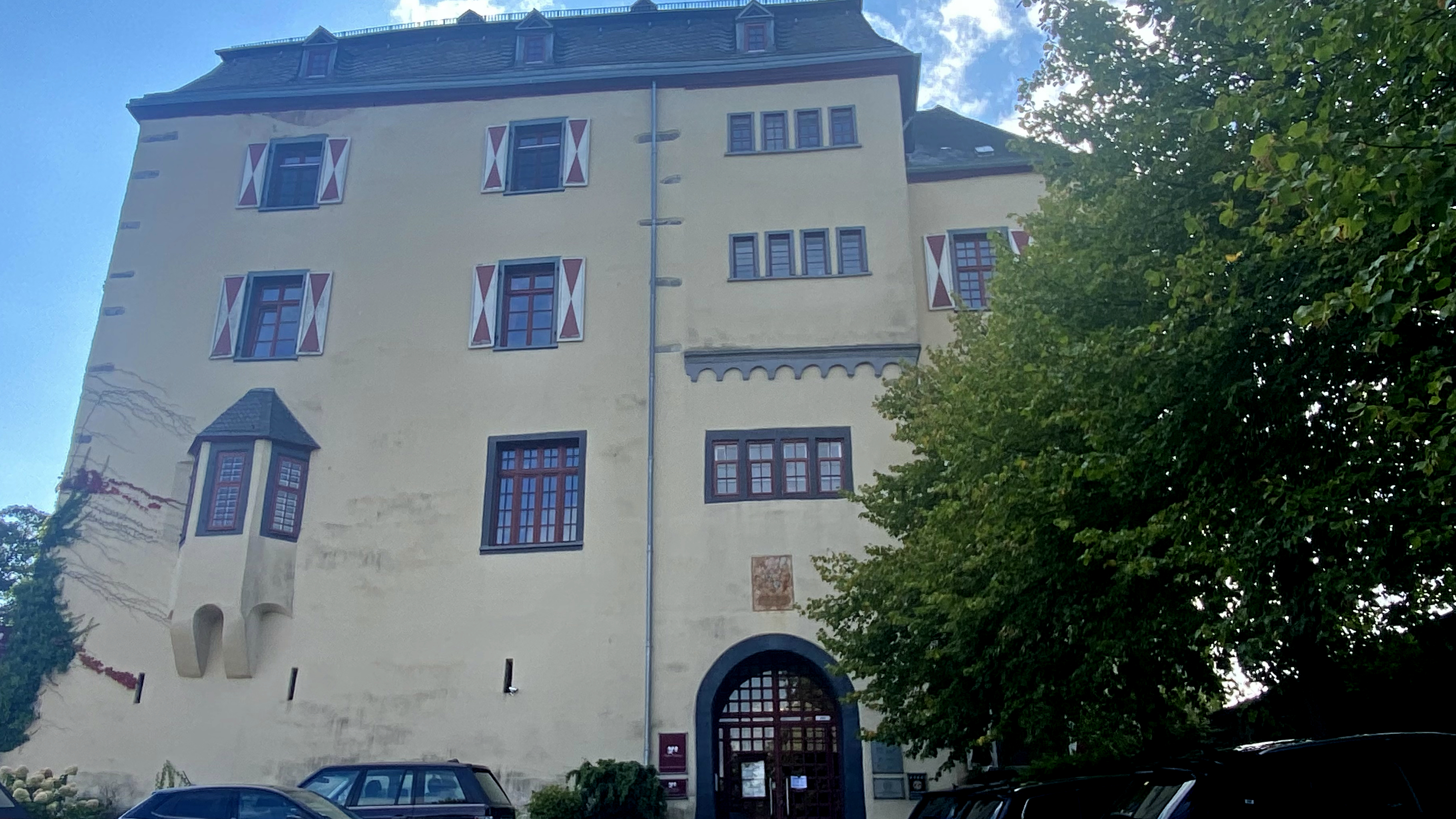 Schloss Westerburg, Sitz des Gewerbevereins Westerburger Land e.V., mit gelber Fassade, roten Fensterläden und arched Eingang, umgeben von Bäumen und Parkplätzen.