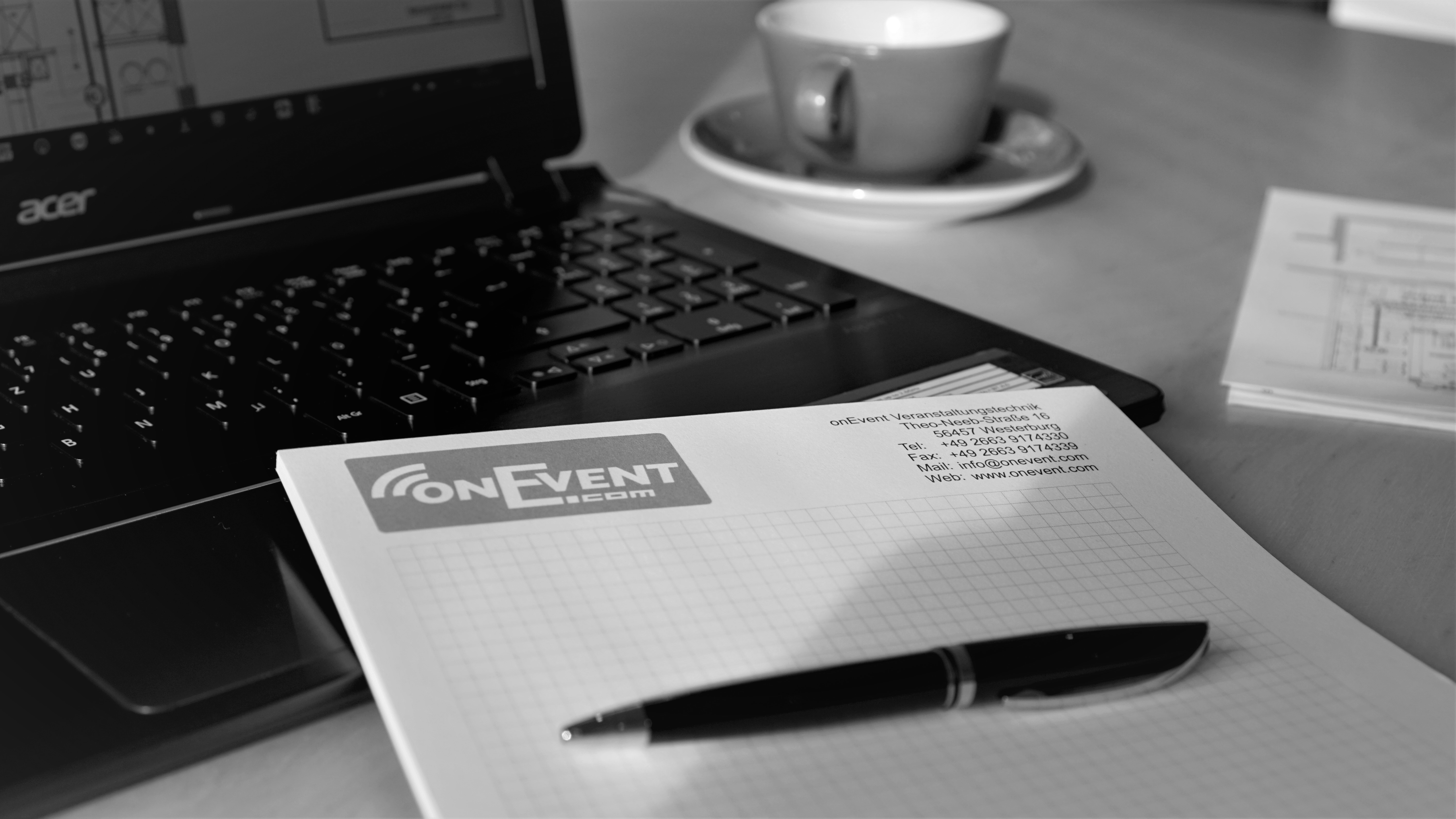 Büroarbeitsplatz mit Acer-Laptop, onEvent-Notizblock (Kontaktdaten), Stift und Kaffeetasse – Abbildung eines typischen Arbeitsumfelds regionaler Unternehmen aus der Verbandsgemeinde Westerburg.