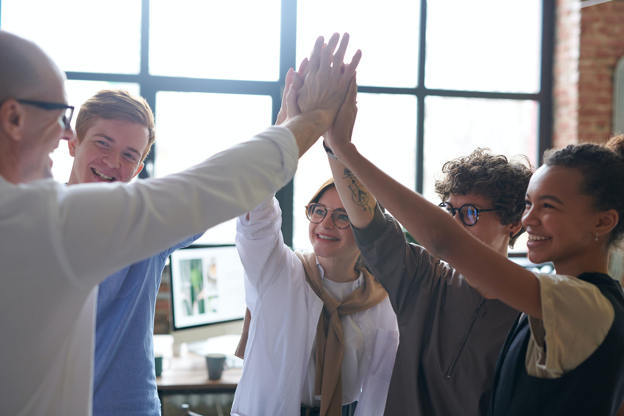 Gruppe von Menschen im Büroumfeld, die sich freudig die Hände hochfünfend gratulieren – Symbol für Teamwork, Erfolg und die Stärkung des regionalen Wirtschaftsstandorts Westerburg.